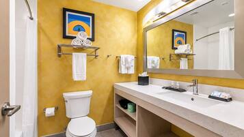 A bathroom with a toilet, sink, and mirror. There are towels and a picture on the wall.