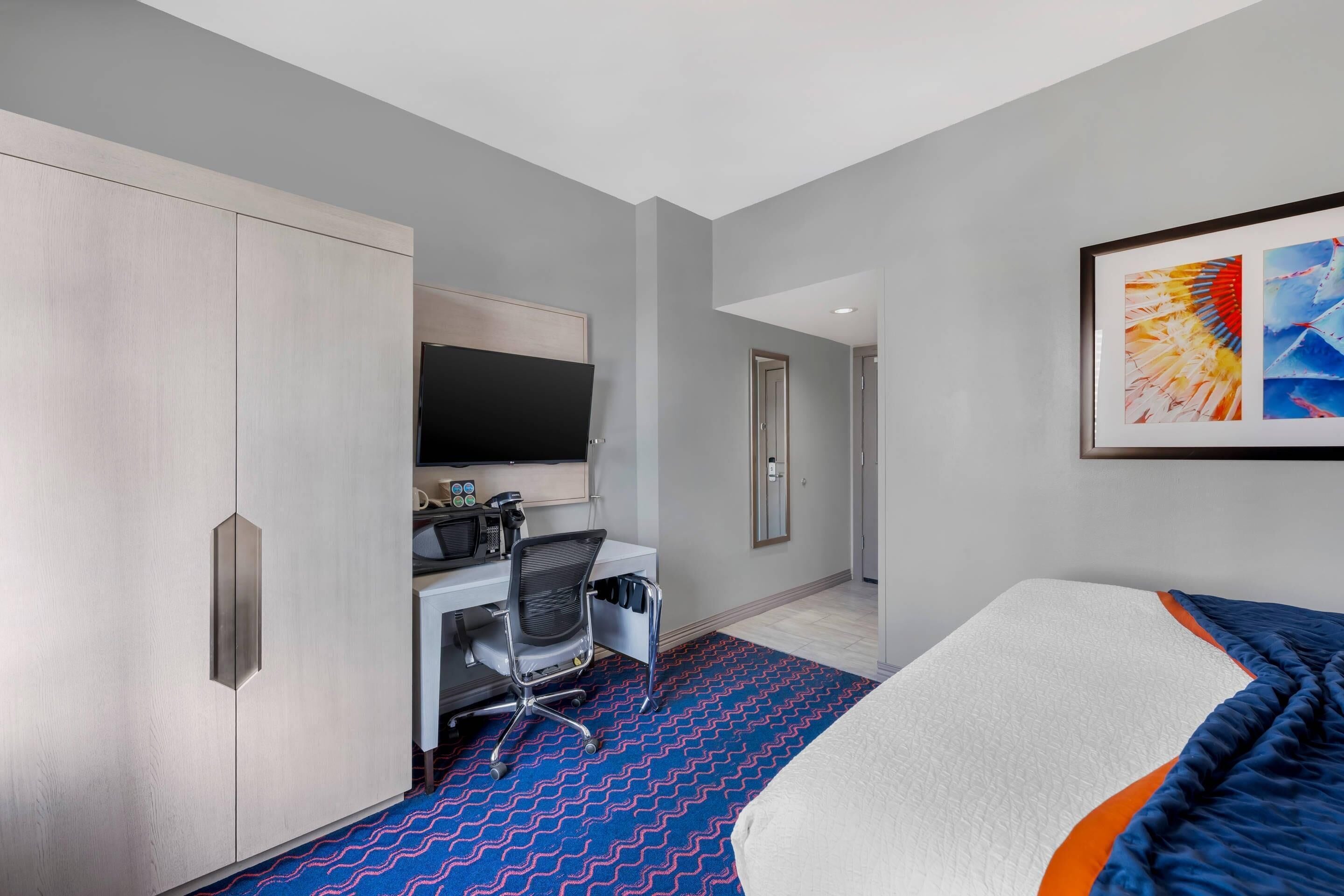 Una habitación de hotel con cama, escritorio, silla, televisor y armario.