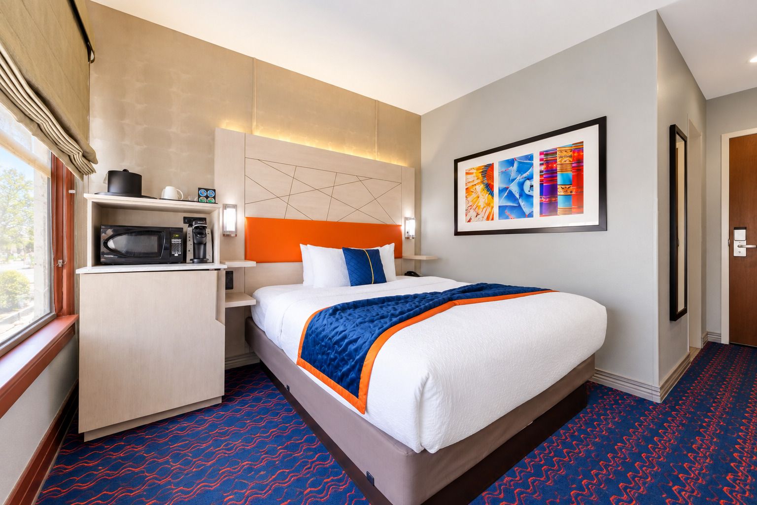 A hotel room with a bed, a microwave, a coffee maker, and a wall-mounted artwork.