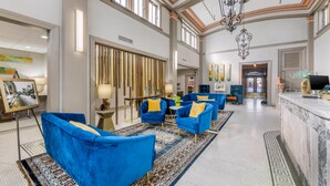 Een ruime lobby met blauwe fauteuils, een receptiebalie en een grote kroonluchter.