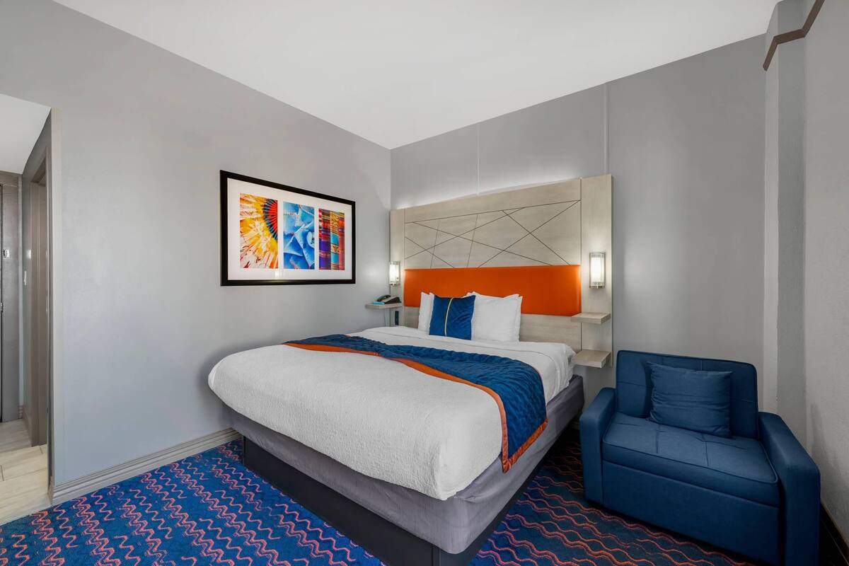 Una habitación de hotel moderna con una cama grande, un sillón azul y una alfombra con estampado geométrico.