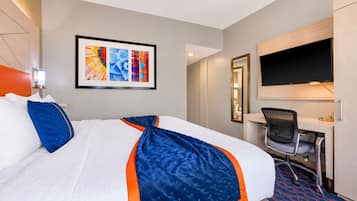 A hotel room with a bed, a desk, a chair, a TV, and a framed artwork on the wall.