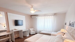 A hotel room with two beds, a desk, a chair, a TV, and a ceiling fan. - Pousada Betânia (Gramado)