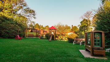 A park with a wooden play structure, benches, and a small building with a red roof.