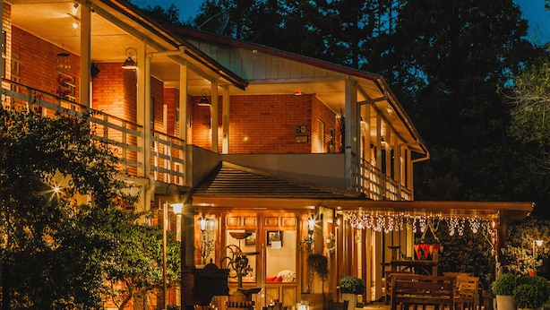 A two-story building with a balcony and outdoor seating area, surrounded by trees. - Pousada Betânia (Gramado)