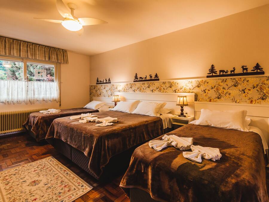 Habitación de hotel con tres camas, un radiador, una ventana con cortinas y un diseño de papel tapiz floral.
