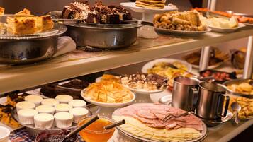 A buffet with various food items including cakes, pastries, and a variety of cheeses and meats.