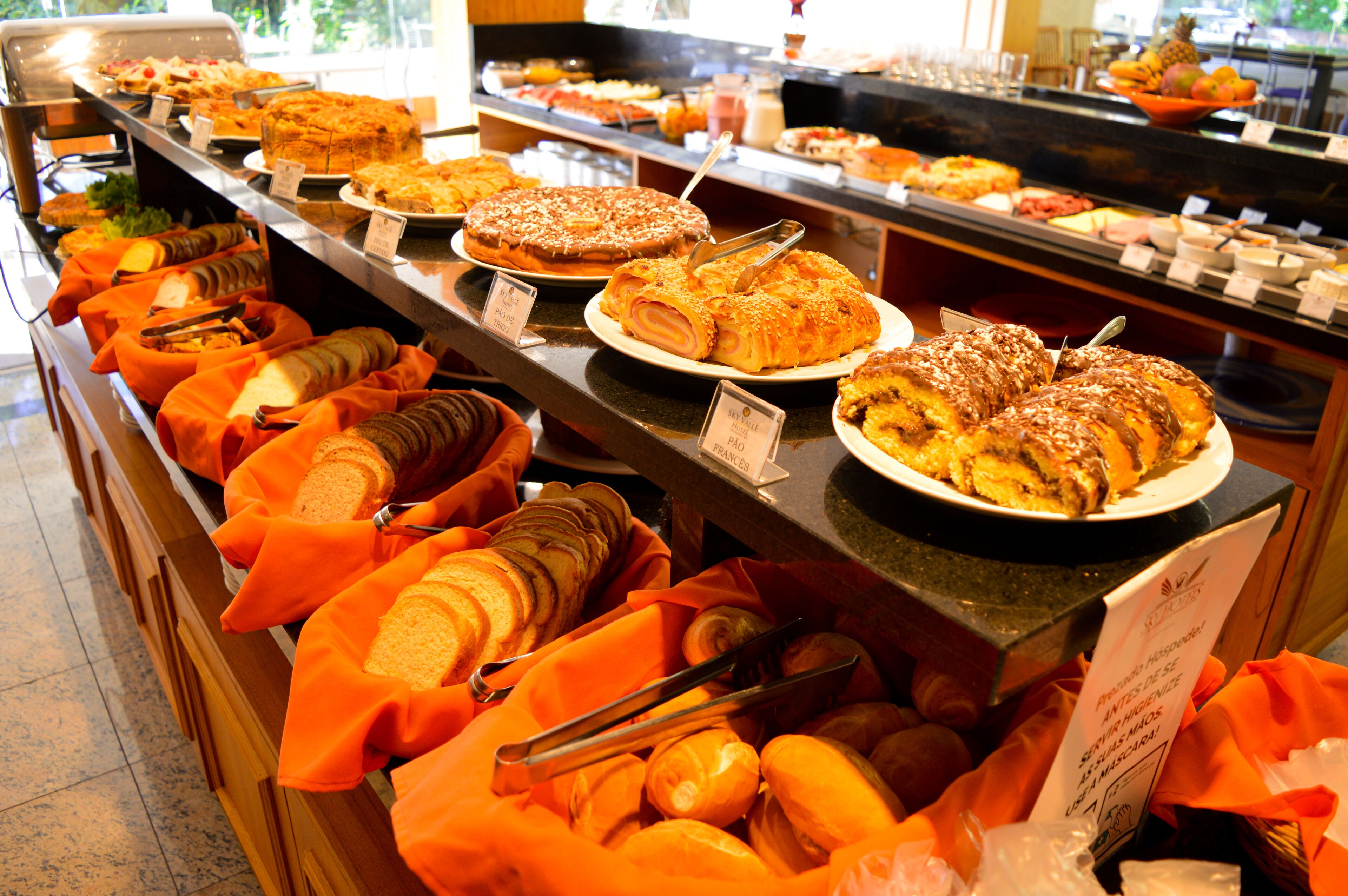 Un bufé con diversos alimentos, entre ellos pan, pasteles y postres, dispuesto en una barra.