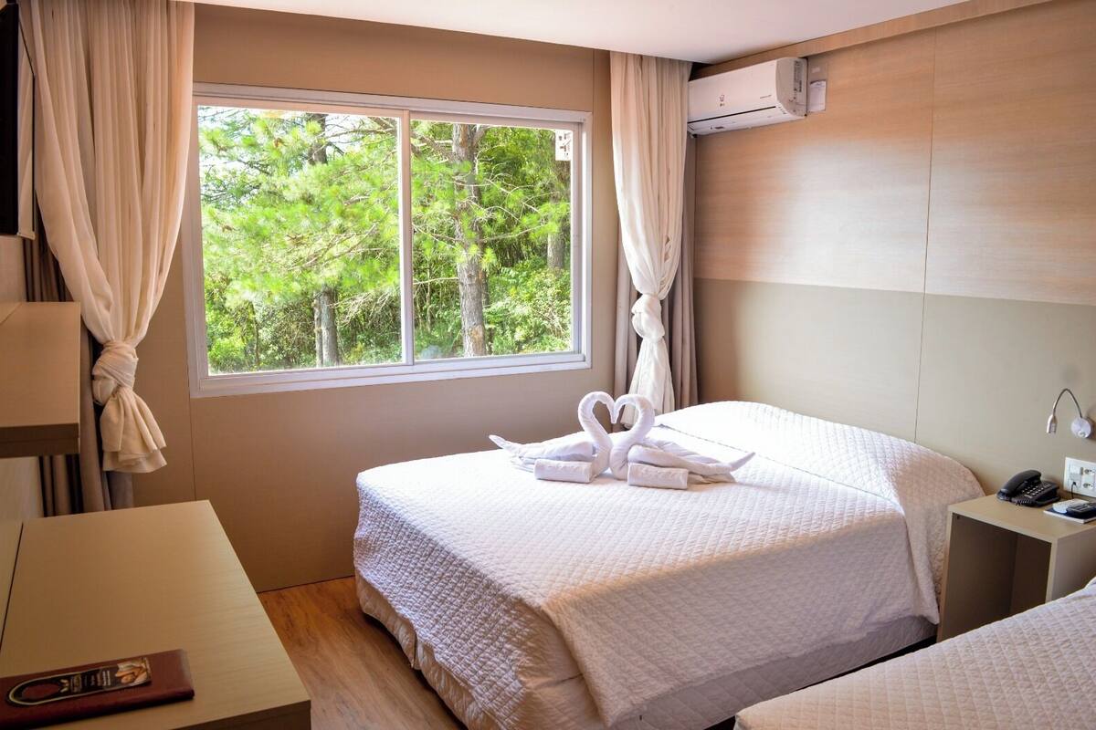 Une chambre d’hôtel comprenant un lit, une table de chevet avec un téléphone et une lampe, une fenêtre avec des rideaux et un appareil de climatisation.