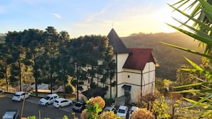 A building with a red roof and white walls, surrounded by trees and parked cars. - Sky Valle Hotel (Gramado)