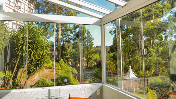 A conservatory with a glass roof, offering a view of a lush garden and a building in the background. - Sky Valle Hotel (Gramado)