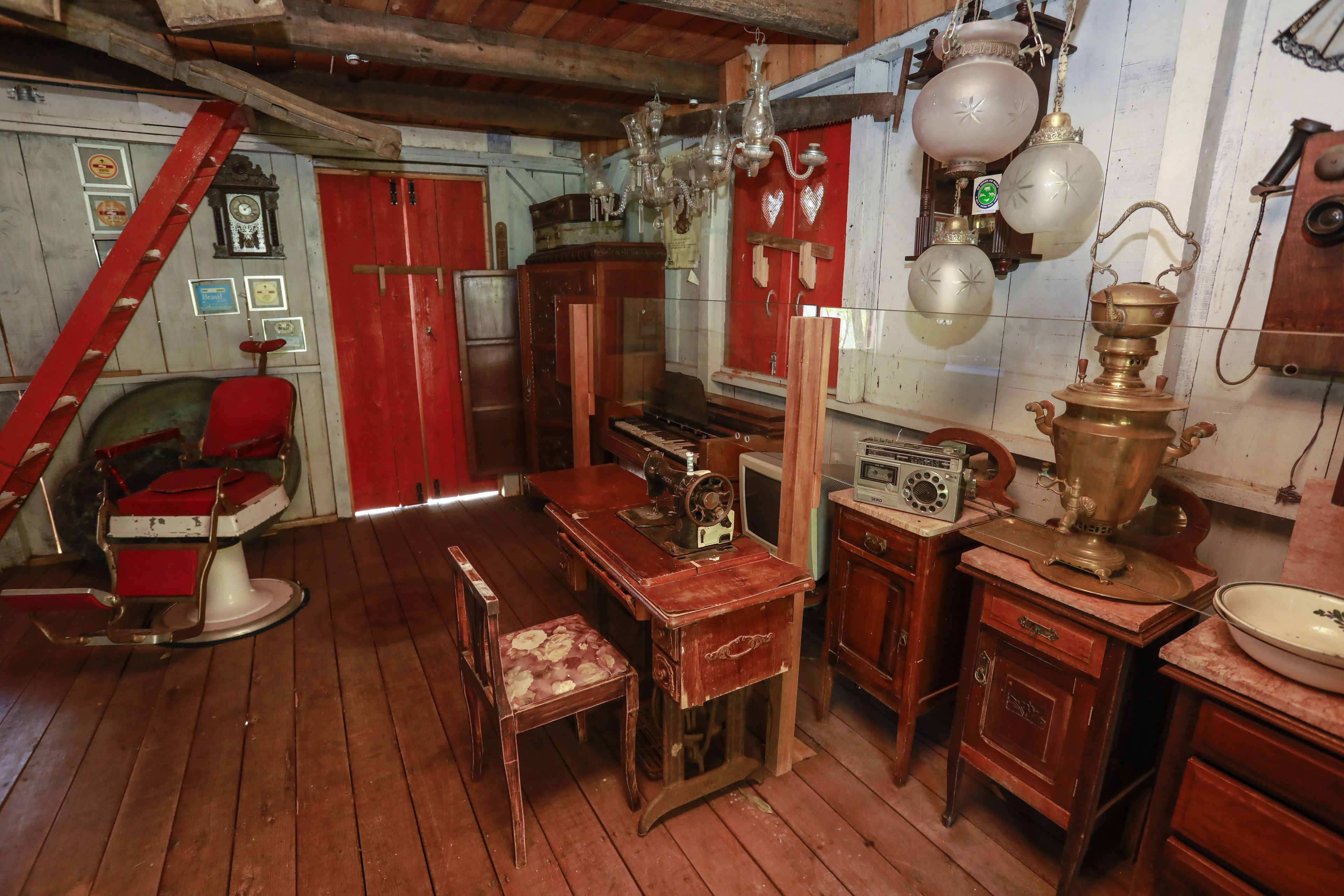 A vintage room with wooden floors, a red chair, a wooden desk, a sewing machine, and a radio.