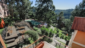 A balcony with a wooden deck, a view of a tennis court, and surrounding greenery. - Sky Valle Hotel (Gramado)