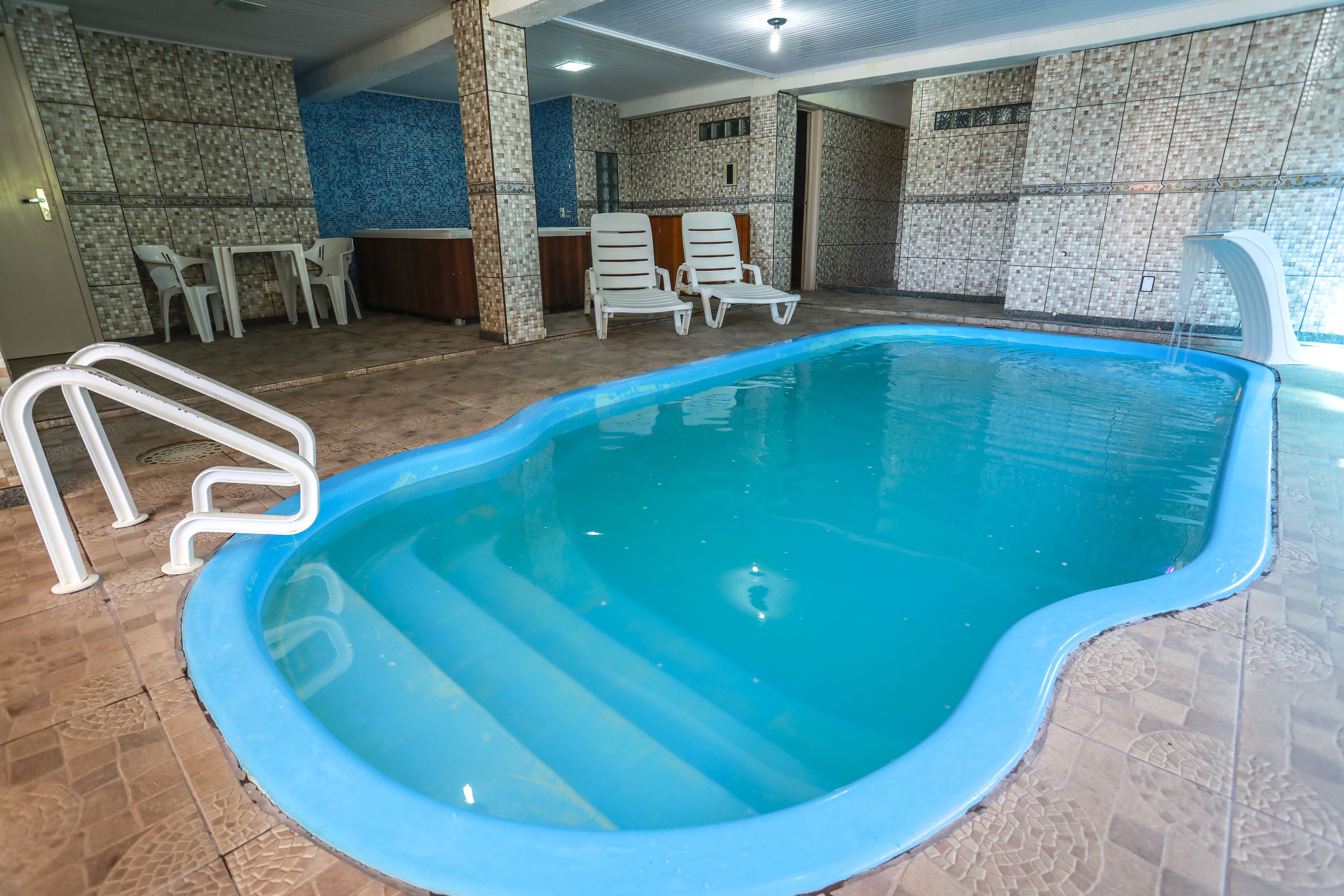 An indoor swimming pool with a blue border, white lounge chairs, and a tiled wall with a blue pattern.