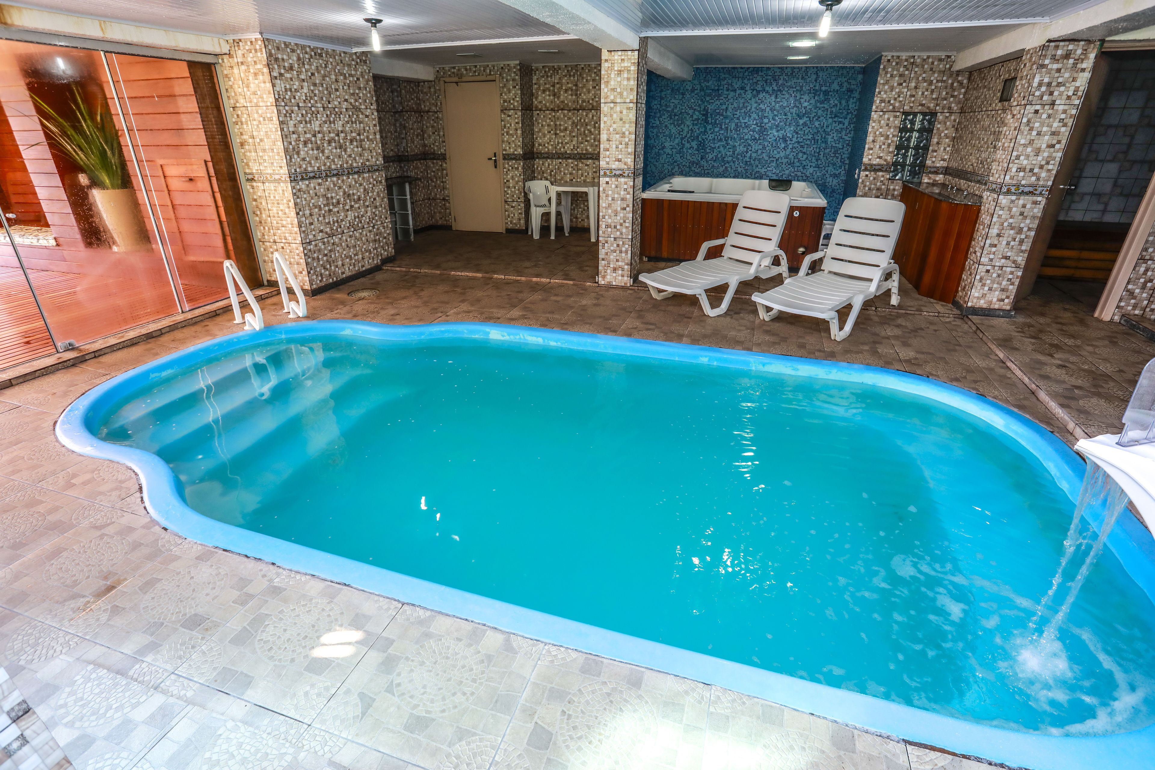 An indoor swimming pool with a tiled floor, a bar area, and lounge chairs.