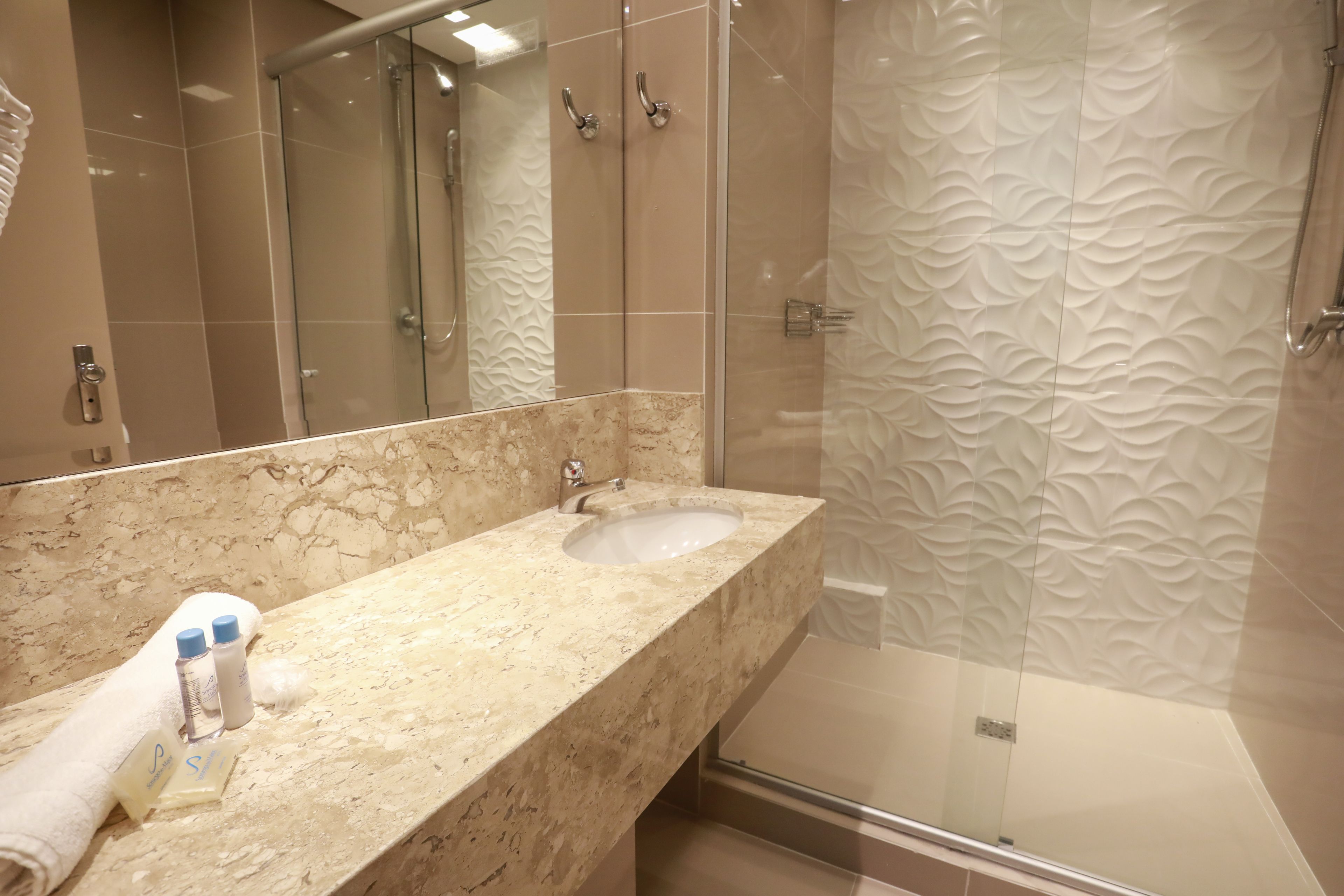 A modern bathroom with a marble vanity, a glass shower enclosure, and a textured wall design.