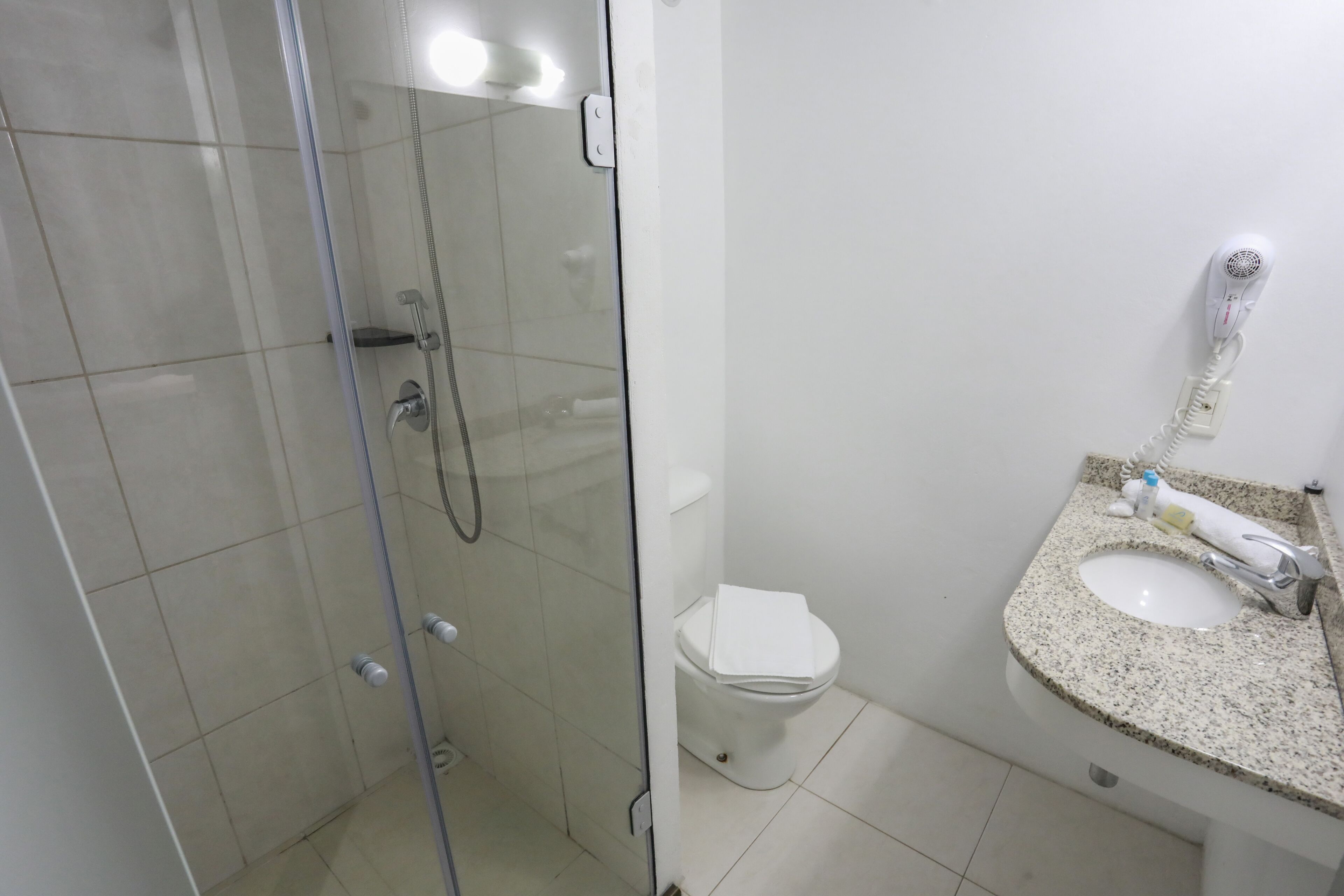 Een badkamer met een douche in een glazen cabine, een toilet en een wastafel met granieten blad.