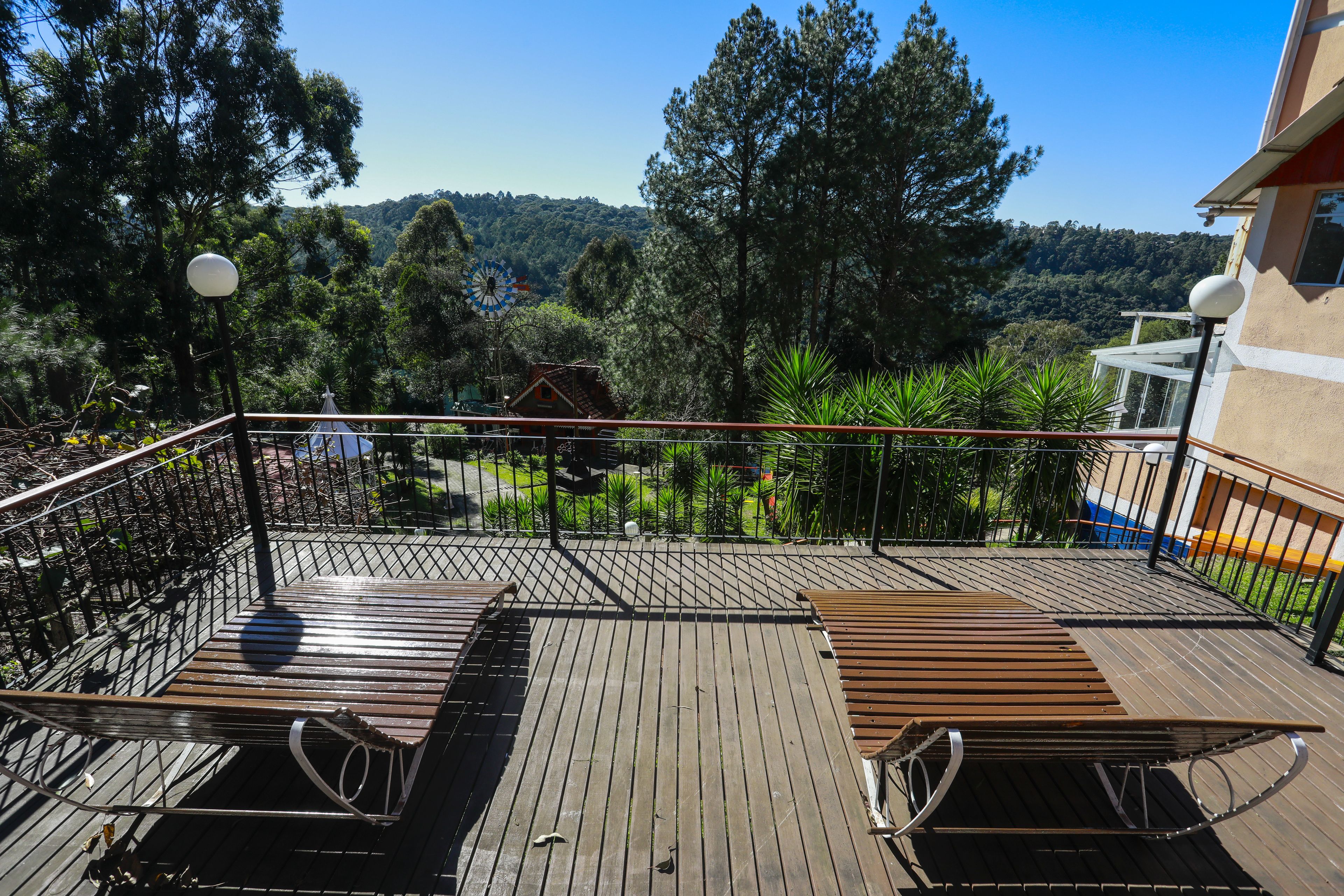A wooden deck with a table and chairs, overlooking a lush landscape with trees and a hill in the distance.