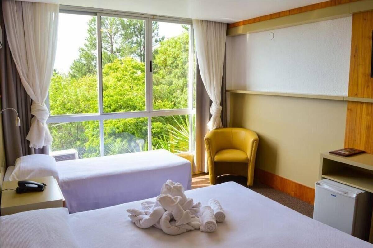 Une chambre d’hôtel avec un lit, une chaise, un bureau avec une lampe et une vue sur la verdure.