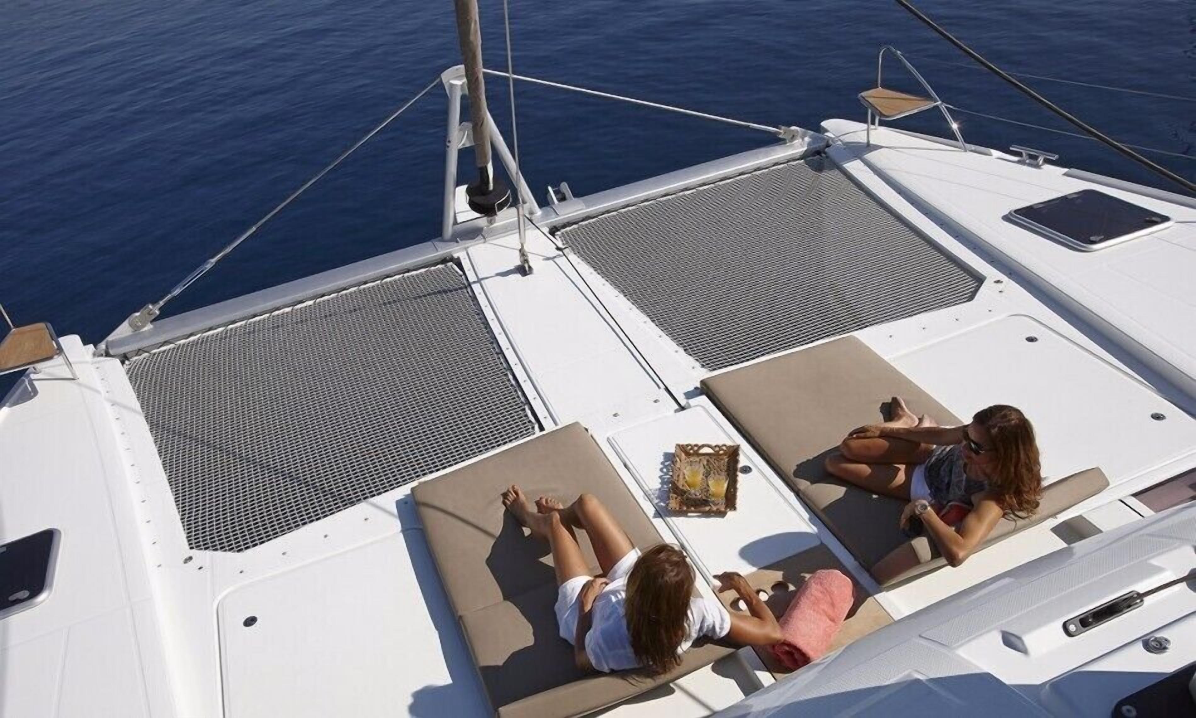 A boat deck with two sun loungers, a small table with a drink, and a view of the sea.
