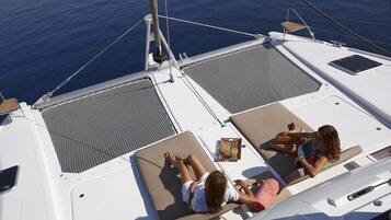 A boat deck with two sun loungers, a small table with a drink, and a view of the sea.