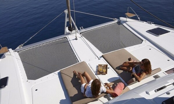 A boat deck with two sun loungers, a small table with a drink, and a view of the sea.