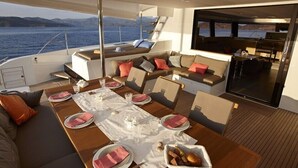Cubierta de un yate con comedor, asientos y vista al mar.