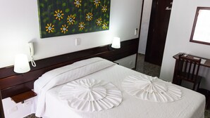 Ein Hotelzimmer mit einem Bett, einem Nachttisch, einer Lampe, einem Bild an der Wand und einer Tür im Hintergrund.