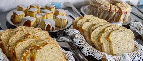 A variety of breads and pastries on display, including sliced bread, a loaf of bread with sesame seeds, and a cake with icing.