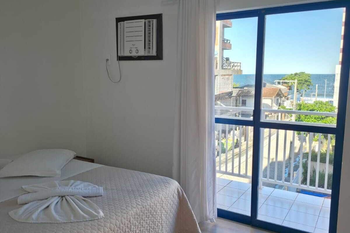 A hotel room with a bed, a view of the city through a balcony, and a wall-mounted air conditioning unit.