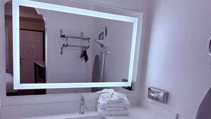 A bathroom with a white sink, a mirror with LED lights, a towel rack, and a towel dispenser. - Travelodge by Wyndham Harbor City (Harbor City)