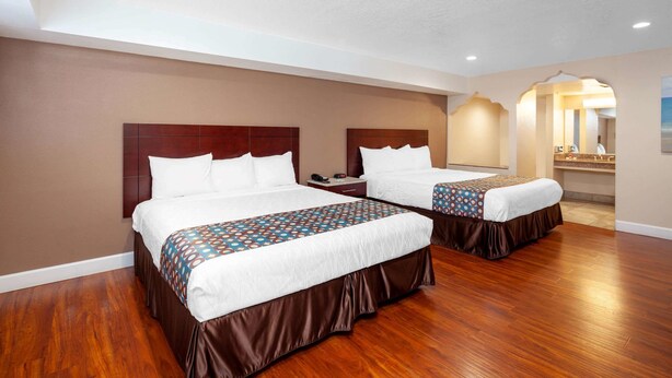 A hotel room with two beds, wooden flooring, and a bathroom visible through an archway. - Travelodge by Wyndham Harbor City (Harbor City)