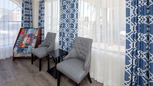 A room with two grey upholstered chairs, a small table, and a display stand with various items. - Travelodge by Wyndham Harbor City (Harbor City)