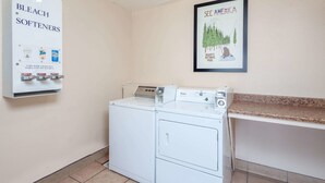 A laundry room with a coin-operated washer and dryer, a sign for bleach softeners, and a framed poster of Yosemite National Park. - Travelodge by Wyndham Harbor City (Harbor City)