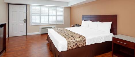 Una habitación de hotel con una cama grande, un escritorio, una silla, un calentador y una puerta.
