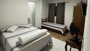 A room with two beds, a desk, a fan, and a mirror. - Pousada Campo Verde (São João del Rei)