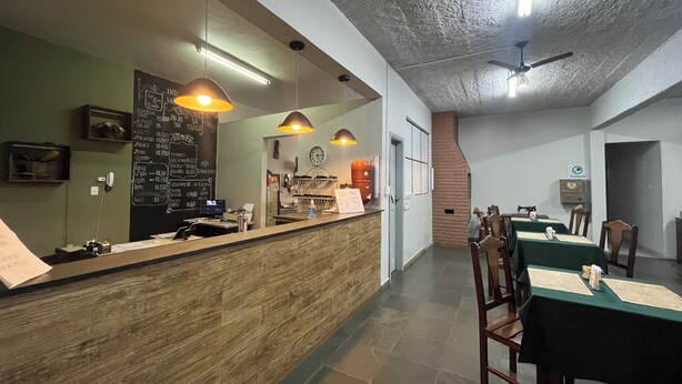 A restaurant interior with a wooden counter, pendant lighting, a chalkboard menu, and a brick wall. - Pousada Campo Verde (São João del Rei)