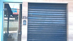 A building entrance with a large metal sign, a closed roller shutter door, and a visible address number. - Pousada Campo Verde (São João del Rei)