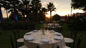 A round table set for six with chairs, surrounded by palm trees and a sunset in the background. - Hotel Misión Express Saltillo (Saltillo)