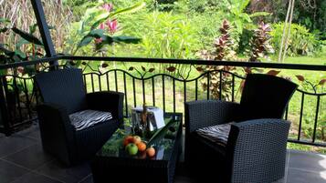 Un balcón con mobiliario de mimbre y una mesa con frutas y una botella.