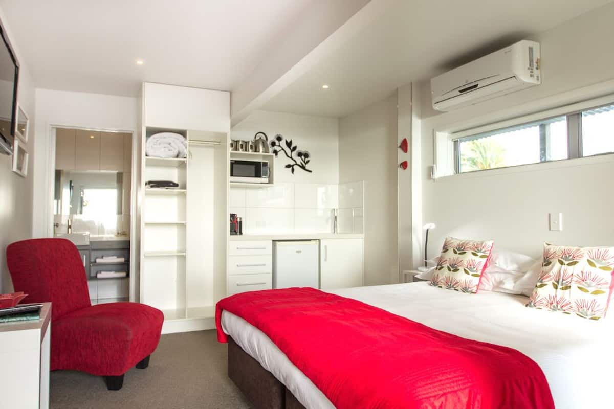 Une chambre moderne avec un grand lit, un fauteuil rouge, une armoire, un four à micro-ondes et un appareil de climatisation.