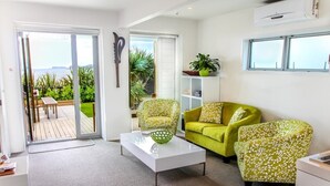 A living room with a glass coffee table, two green patterned armchairs, a white sofa, and a view of the outdoors through a sliding glass door. - Kokomo Retreat (Russell)