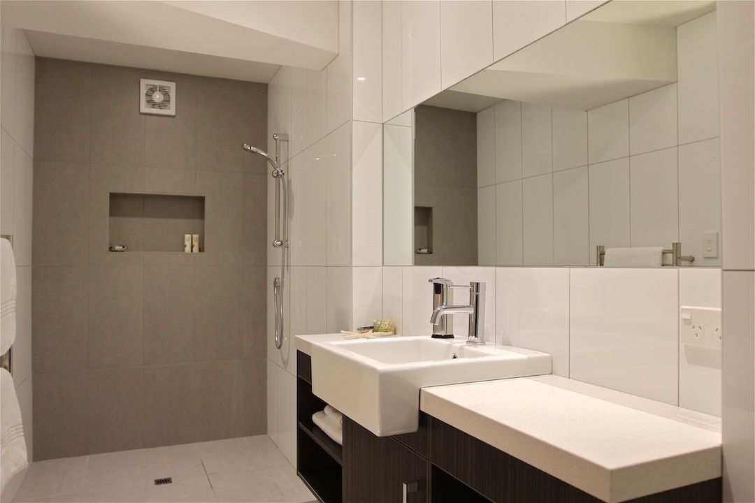 A modern bathroom with a large mirror, two sinks, and a shower.