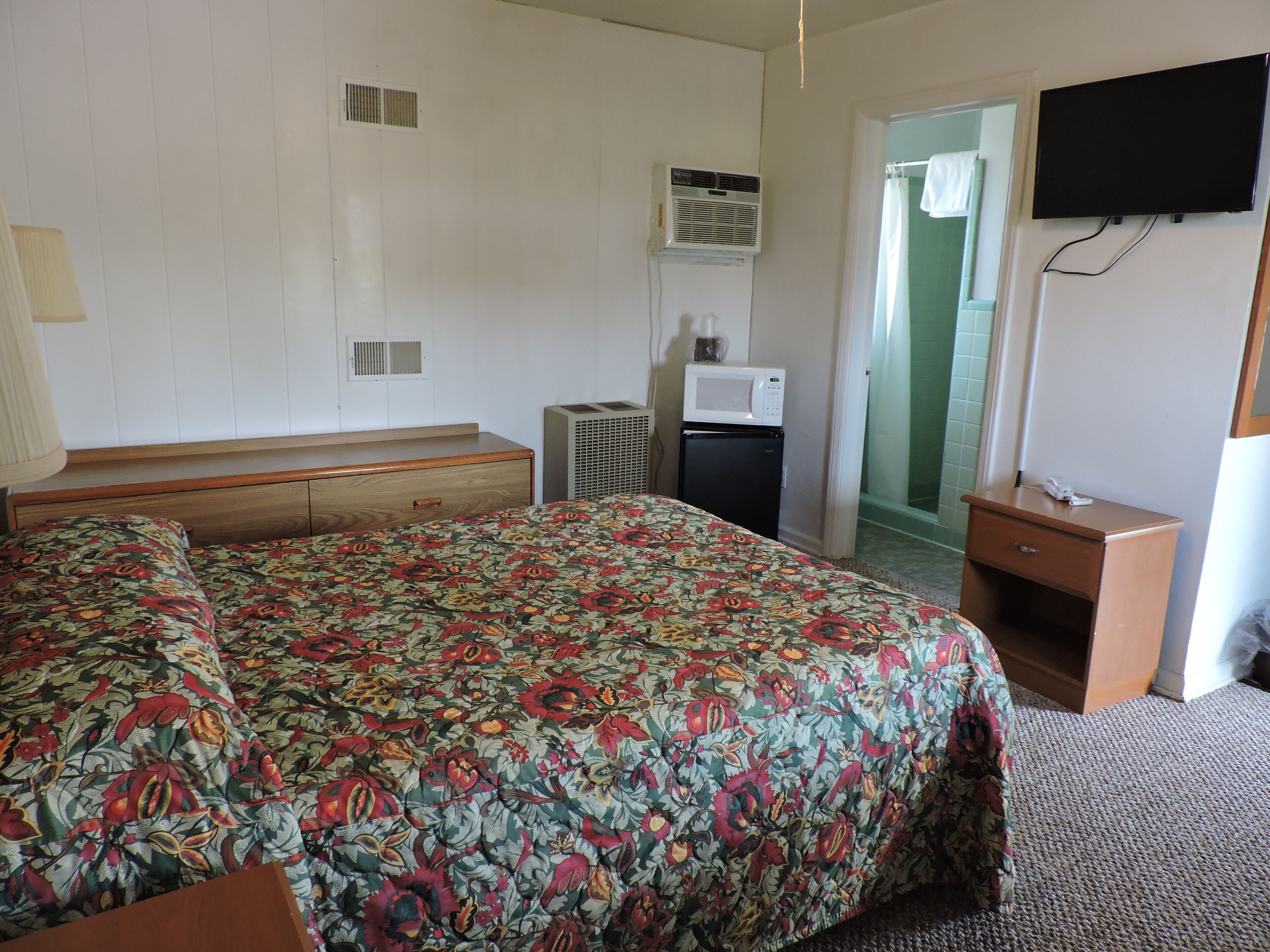 Une chambre d’hôtel équipée d’un lit, d’un petit bureau, d’une télévision, d’un climatiseur et d’un four à micro-ondes.