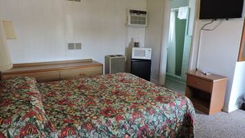 Una habitación de hotel con cama, un escritorio pequeño, televisión, aire acondicionado y microondas.