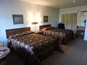A hotel room with two beds, a desk, a chair, a lamp, and a television.
