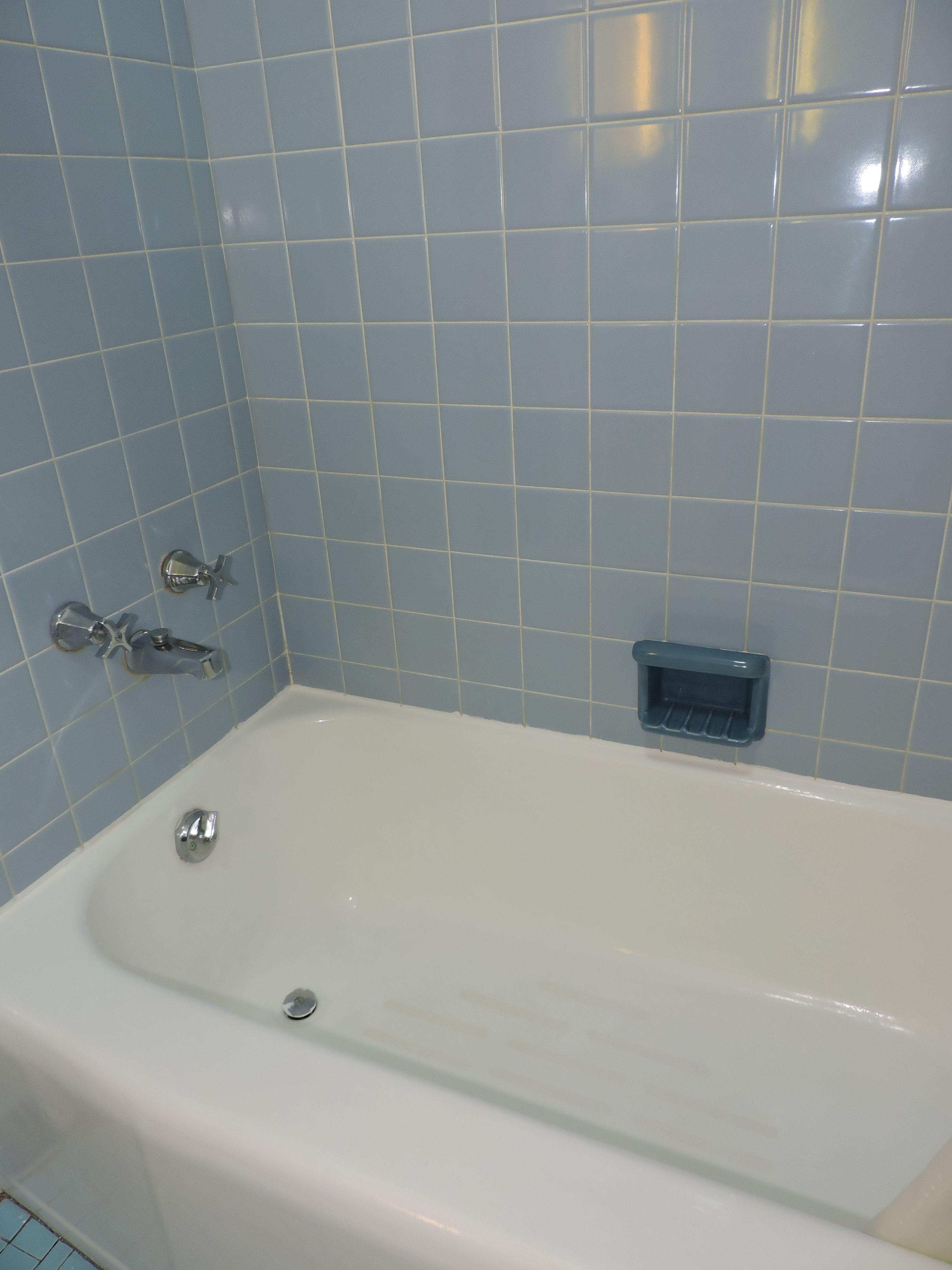 A bathroom with a white bathtub, blue tiled walls, and a blue soap dish.