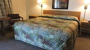 Una camera d'albergo con un letto grande, due abat-jour, una sedia, un tavolino e un quadro appeso al muro.