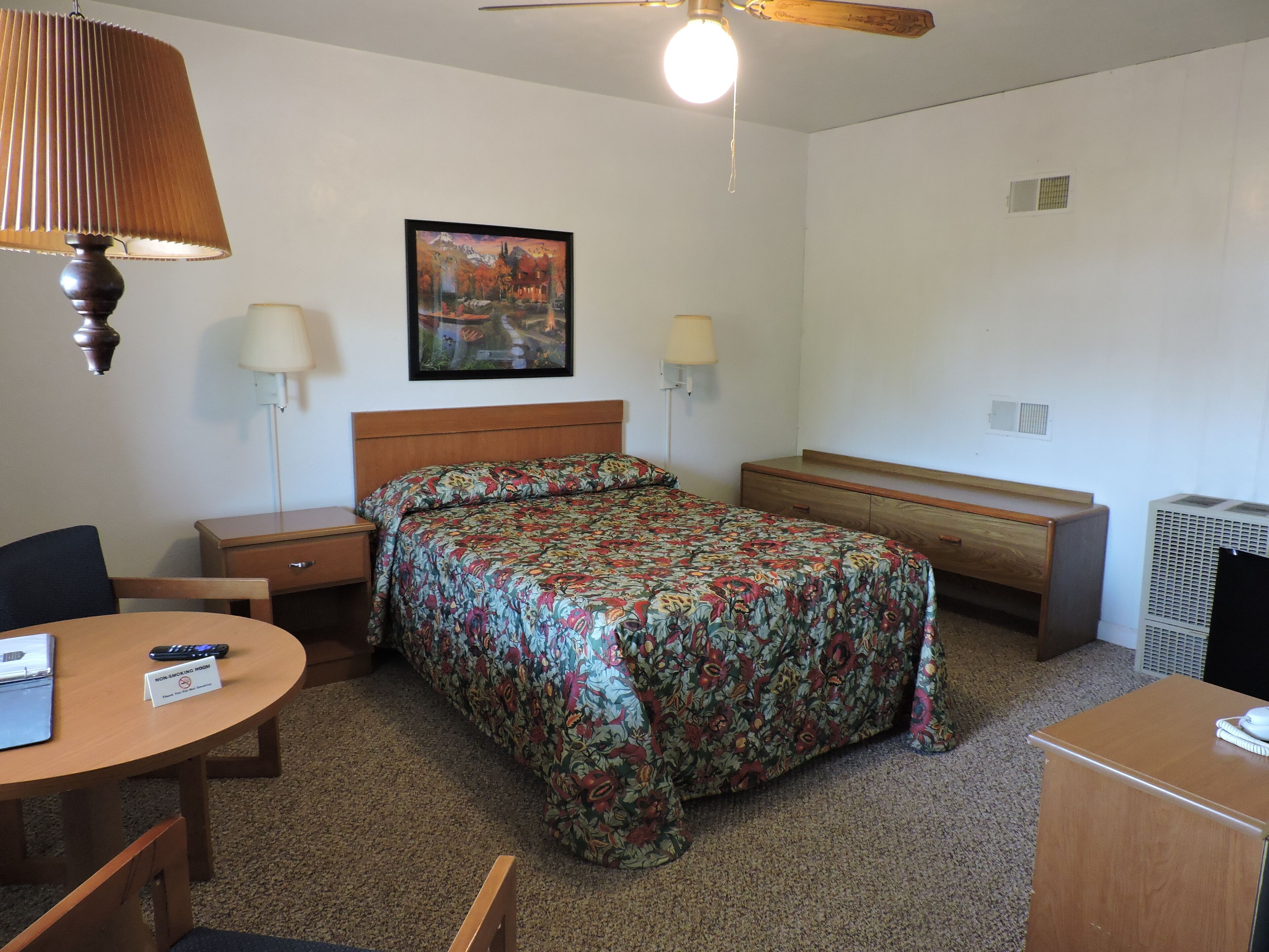 Une chambre d’hôtel équipée d’un lit, de tables de chevet, d’un bureau, d’une chaise, d’un ventilateur de plafond et d’un appareil de climatisation.