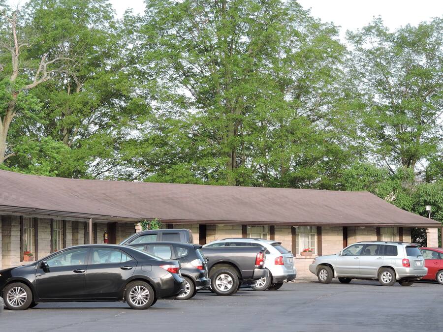 A motel with a row of parked cars in front, surrounded by trees.